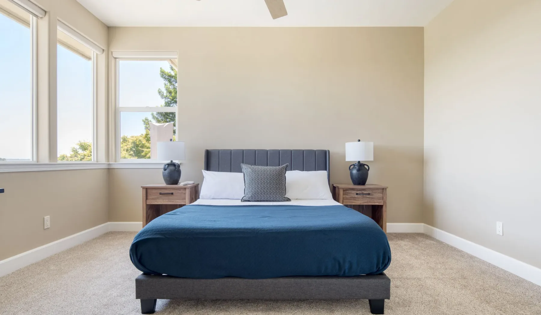Un dormitorio con una cama vestida con ropa de cama azul y ventanas a lo largo de una pared.