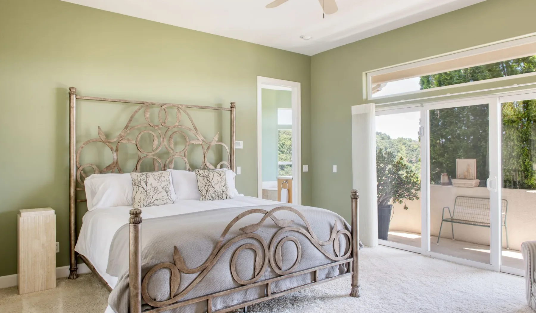 Un dormitorio luminoso con una cama de metal y grandes puertas corredizas de vidrio que dan a un patio.