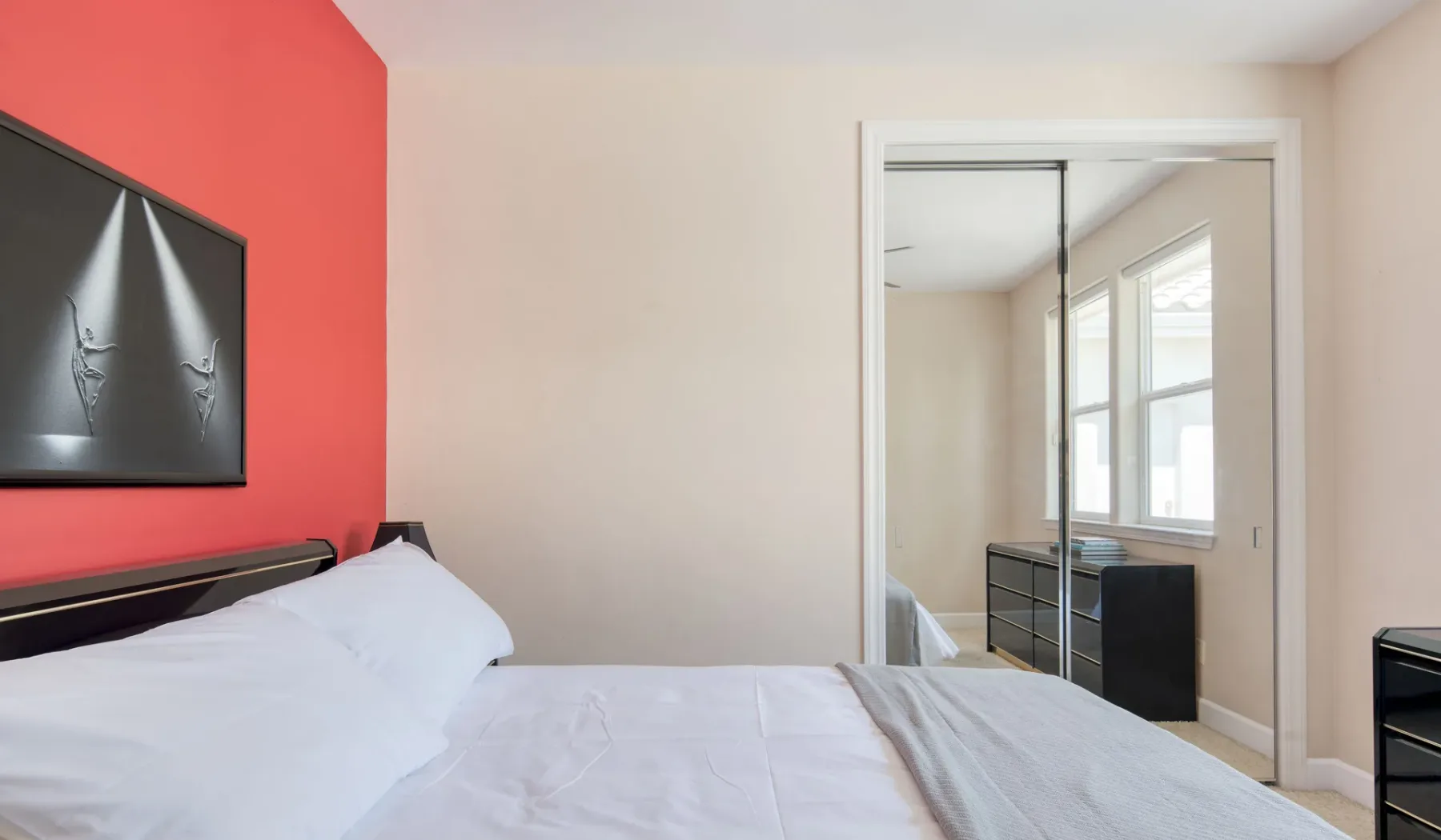 Un dormitorio con una cama junto a una pared de acento roja y un armario con espejo.
