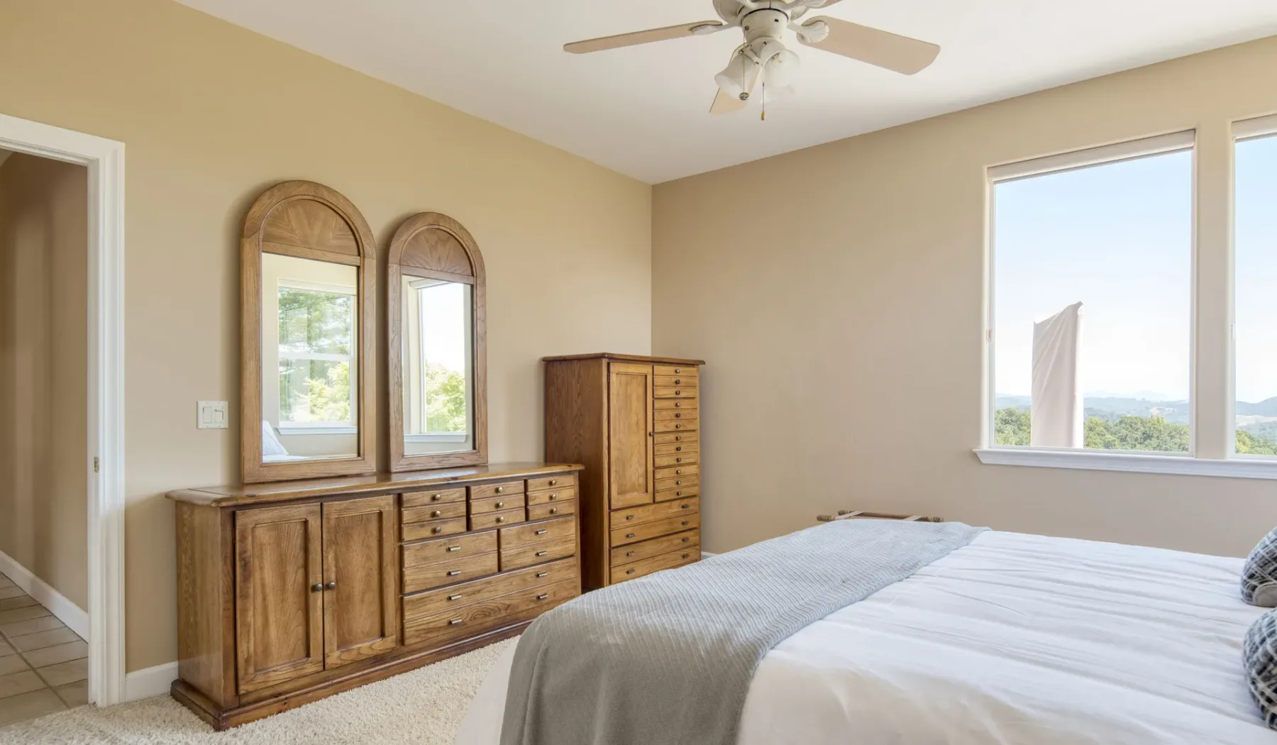 Un dormitorio con una cama, cómodas de madera y ventanas luminosas.