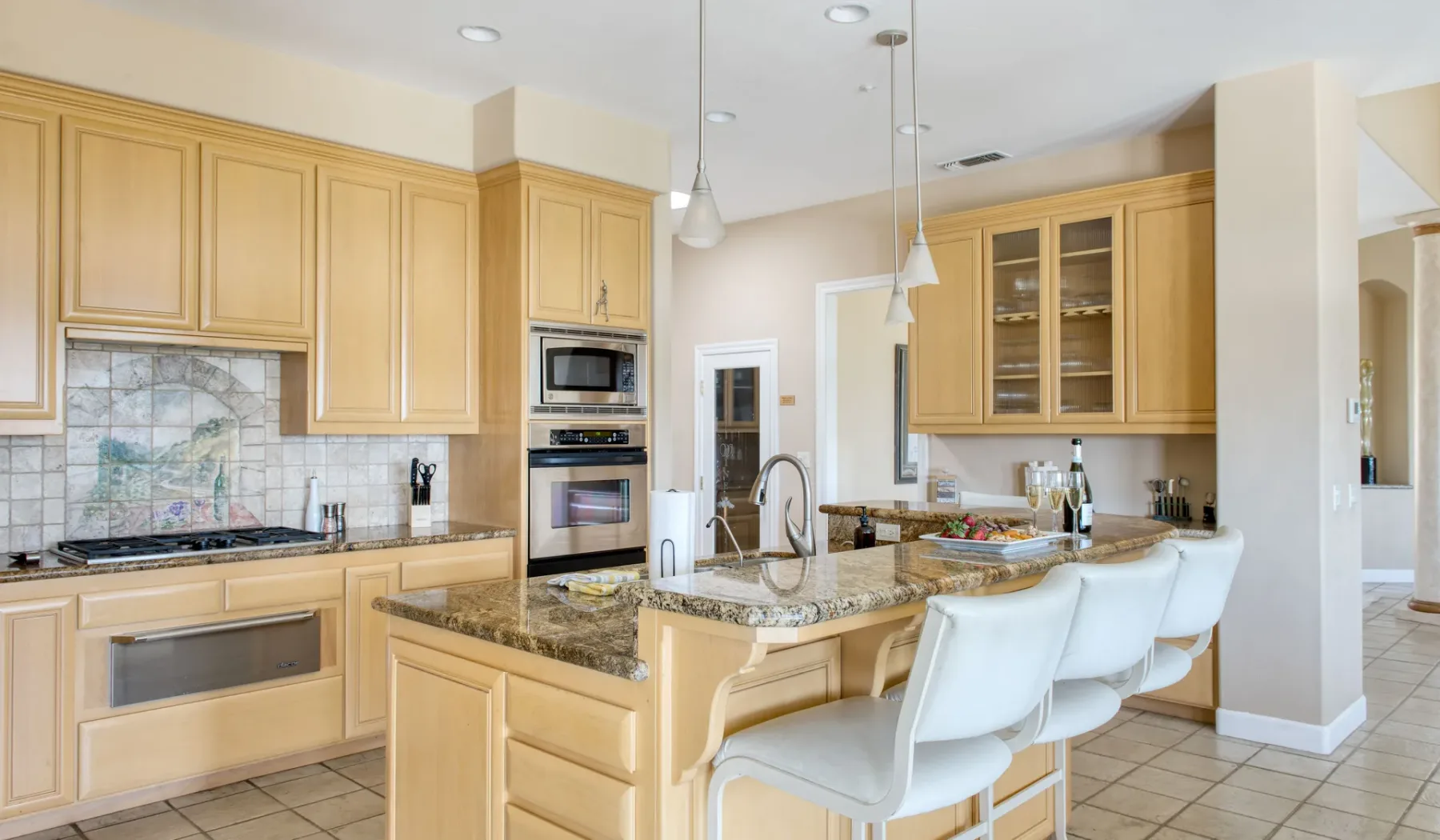 Una cocina luminosa con una isla central, lámparas colgantes y asientos blancos.