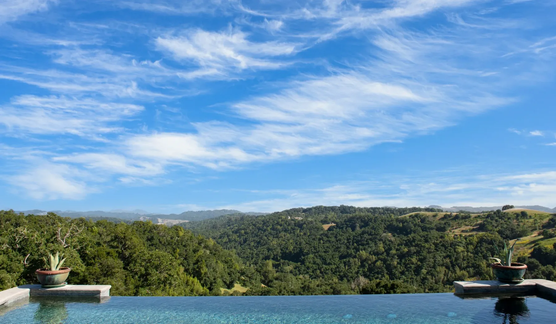 Una piscina exterior ofrece vistas a un paisaje verde y boscoso bajo un cielo azul.