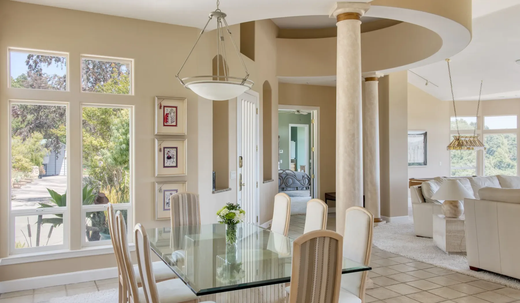 Un comedor con una mesa de vidrio y ventanas altas se abre a una sala de estar.