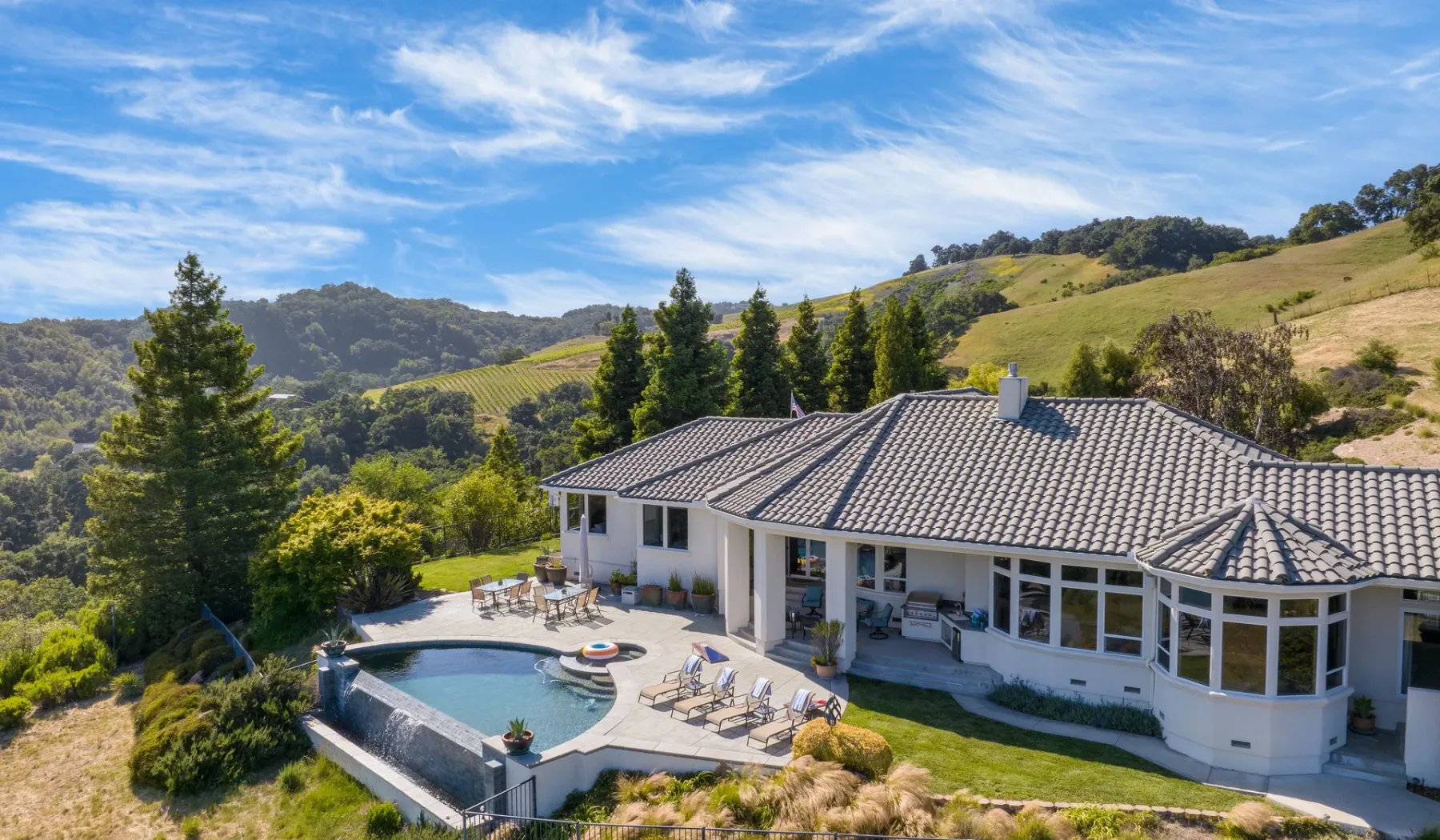 Una casa en una ladera con piscina y colinas verdes alrededor.