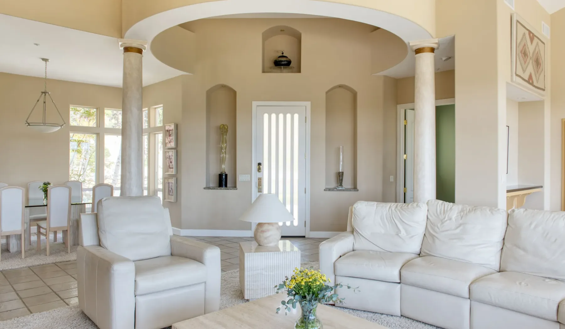 Una sala luminosa con asientos blancos y un comedor contiguo.