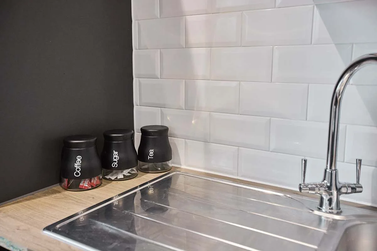Fregadero y encimera de cocina con recipientes etiquetados para café, azúcar y té.