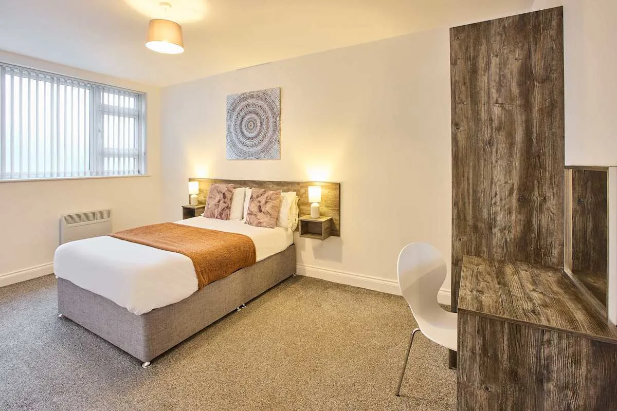Un dormitorio con una cama, mesitas de noche y una ventana con persianas verticales.