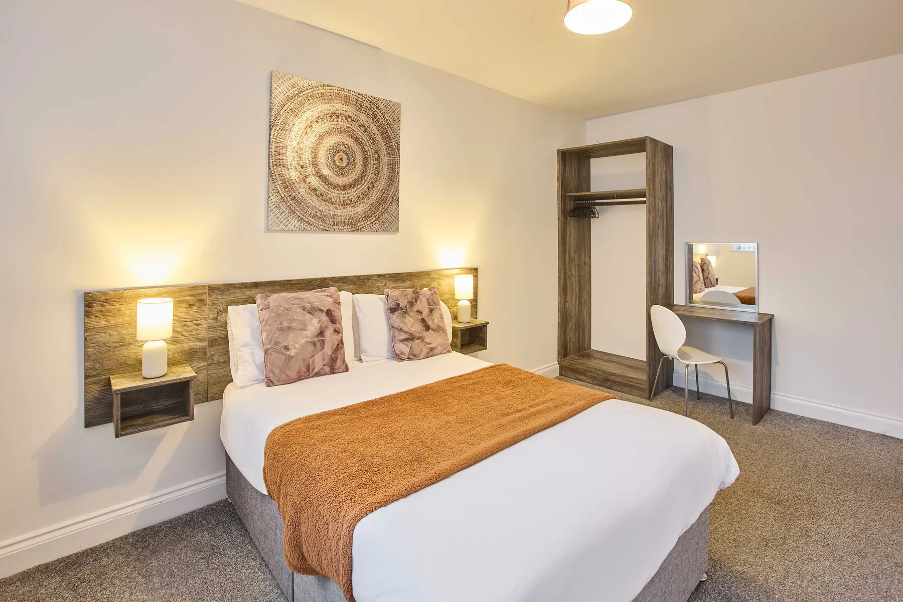 Un dormitorio con una cama, arte en la pared y un pequeño tocador.