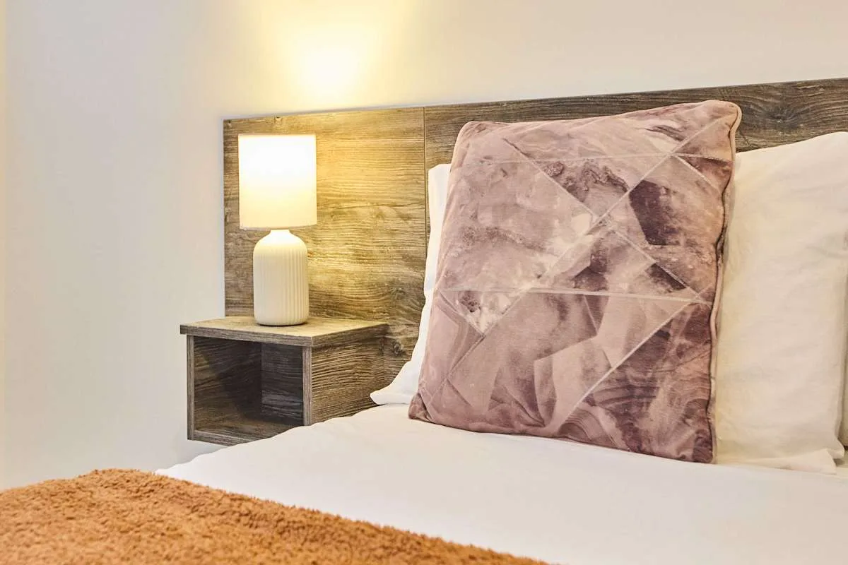 Dormitorio con una cama, un cojín estampado y una lámpara de mesilla.