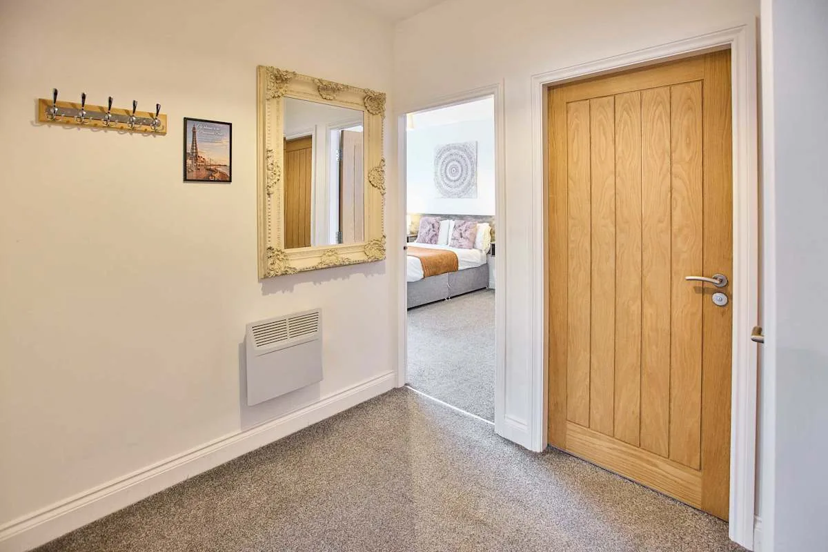 Un pasillo alfombrado conduce a un dormitorio, con una puerta de madera y un espejo.