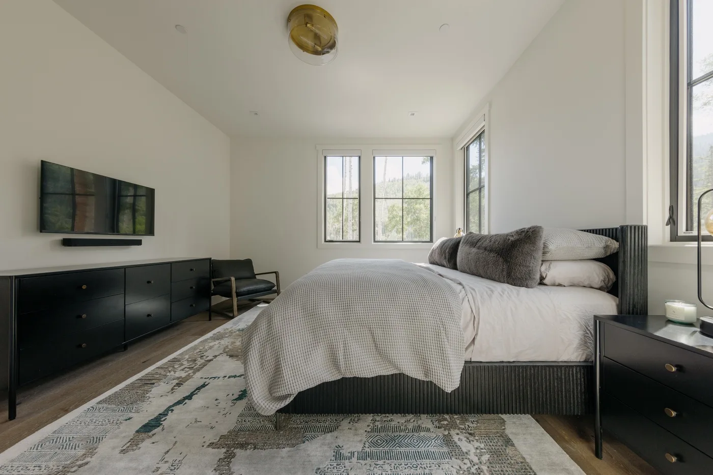 Un dormitorio luminoso con una cama grande, un televisor en la pared y ventanas.