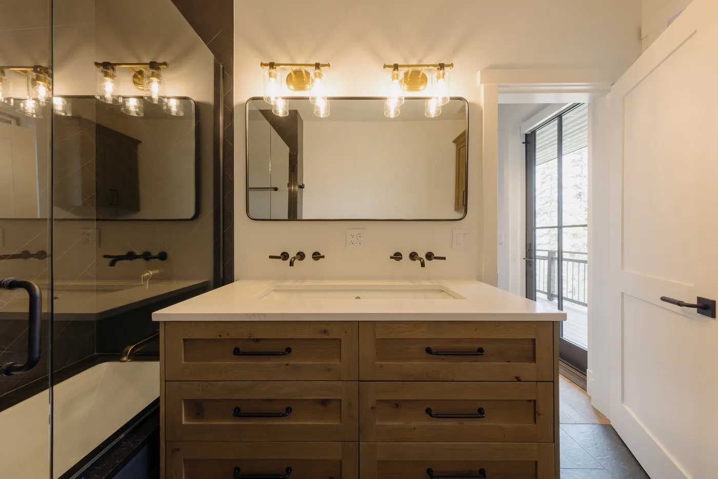 Un tocador de baño con un espejo amplio y una puerta abierta a una habitación luminosa.