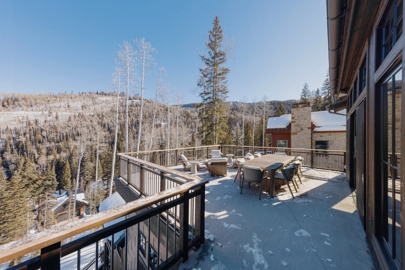 Una terraza exterior con asientos ofrece vistas de un paisaje montañoso nevado y boscoso.