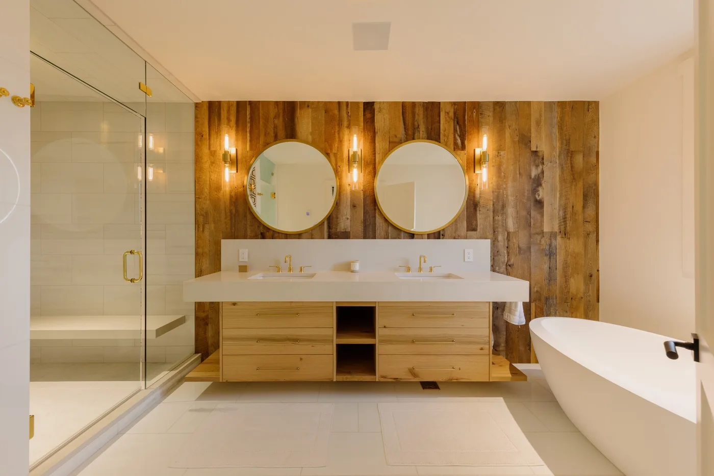 Un baño con lavabo doble, espejos redondos, una ducha de vidrio y una bañera exenta.