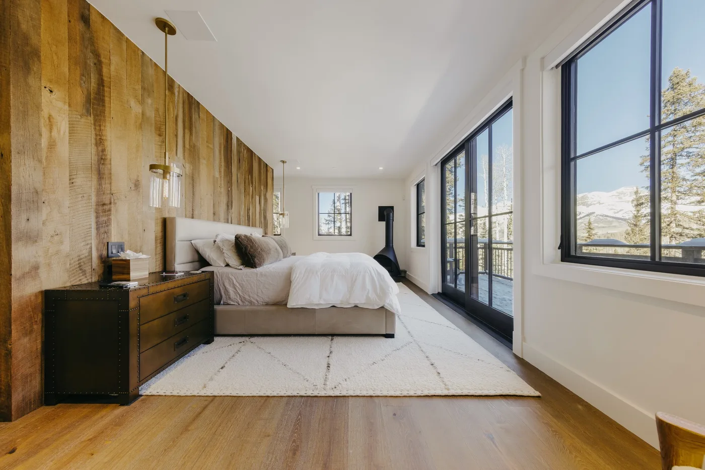 Un dormitorio luminoso con una cama junto a grandes ventanas y una pared revestida de madera.