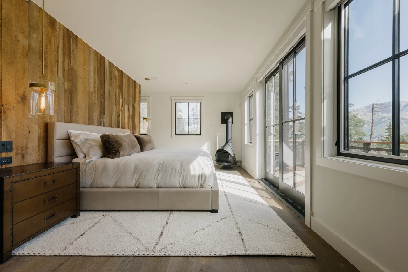 Un dormitorio luminoso con una cama junto a grandes ventanas y una pared revestida de madera.
