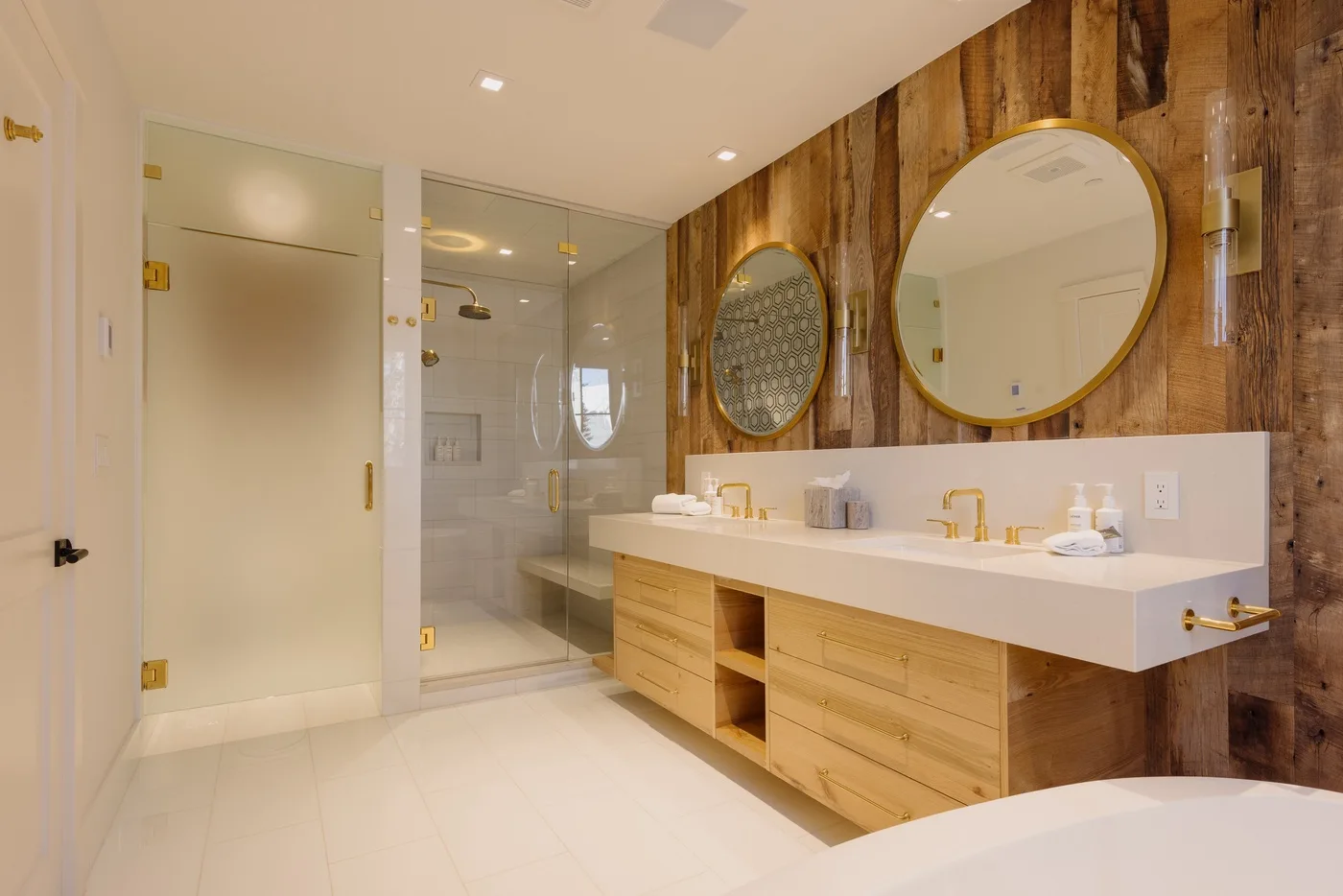 Un baño con un lavabo largo, espejos redondos y una ducha de vidrio.