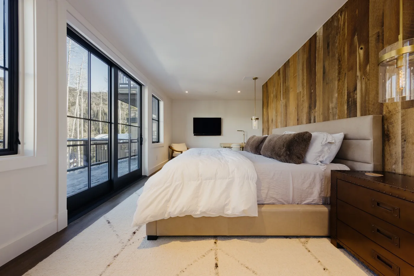 Un dormitorio con una cama, una pared revestida de madera y grandes puertas de vidrio.