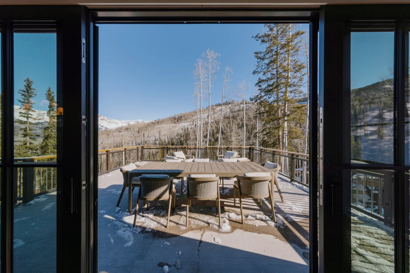 Una mesa de comedor y asientos están en una terraza con vistas a un paisaje montañoso nevado.
