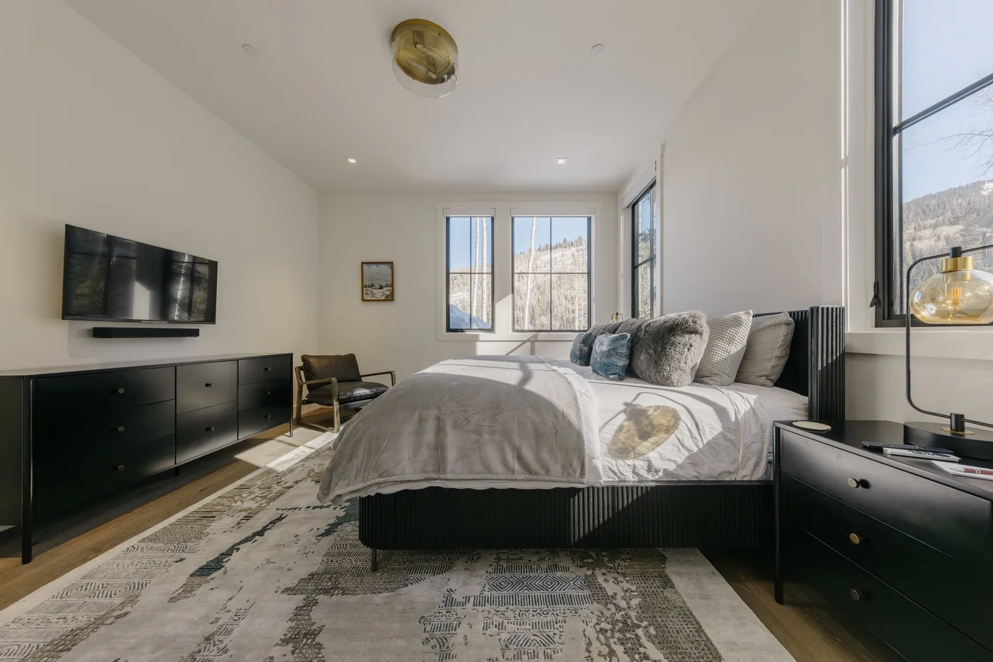 Un dormitorio luminoso con una cama grande, muebles oscuros y ventanas con vistas al paisaje.