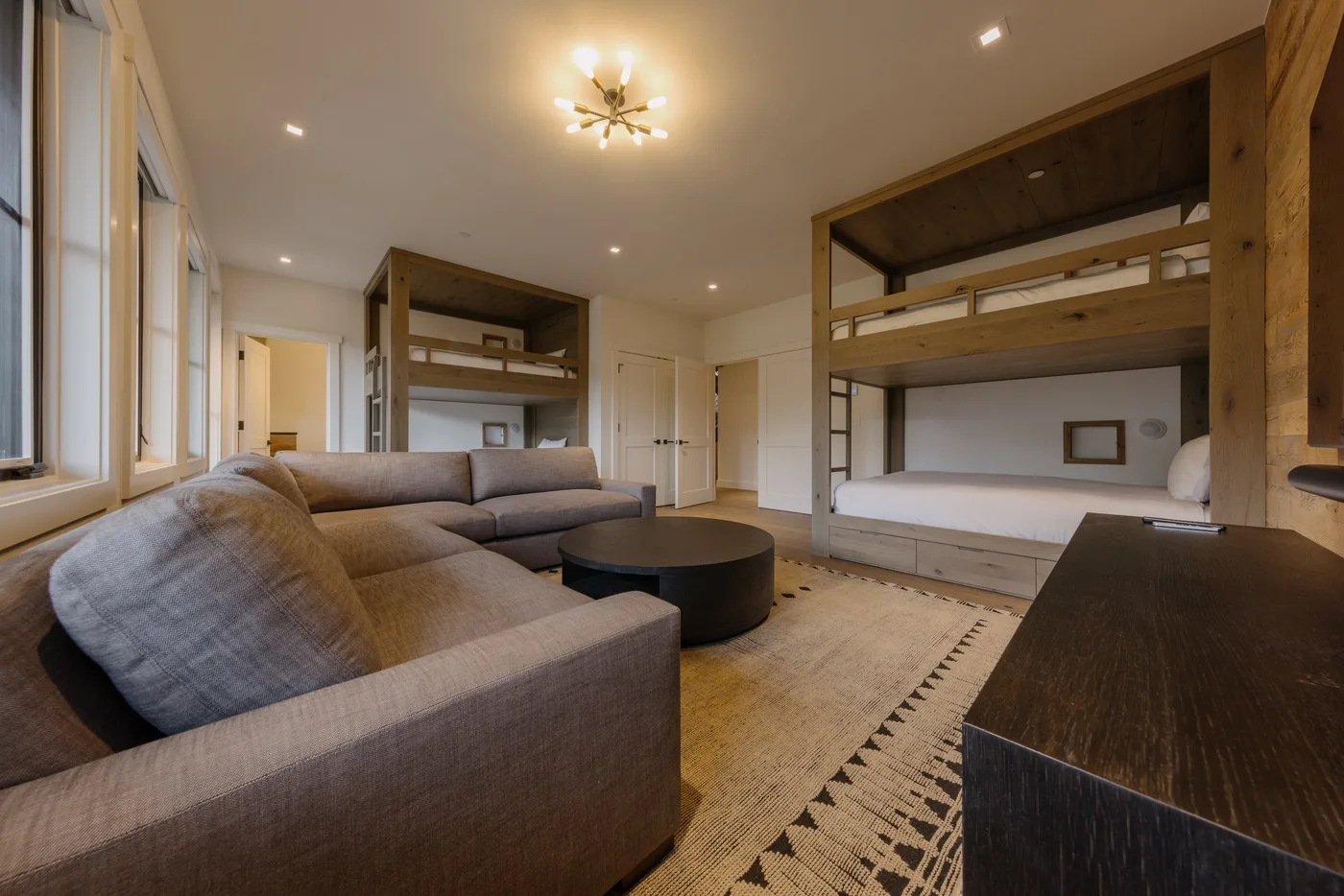 Dormitorio con una zona de asientos gris y literas de madera.