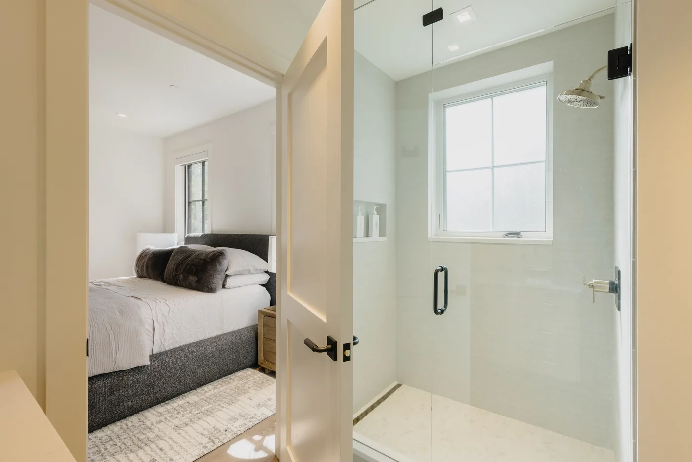 Se ve un dormitorio junto a un baño luminoso con una ducha de vidrio.