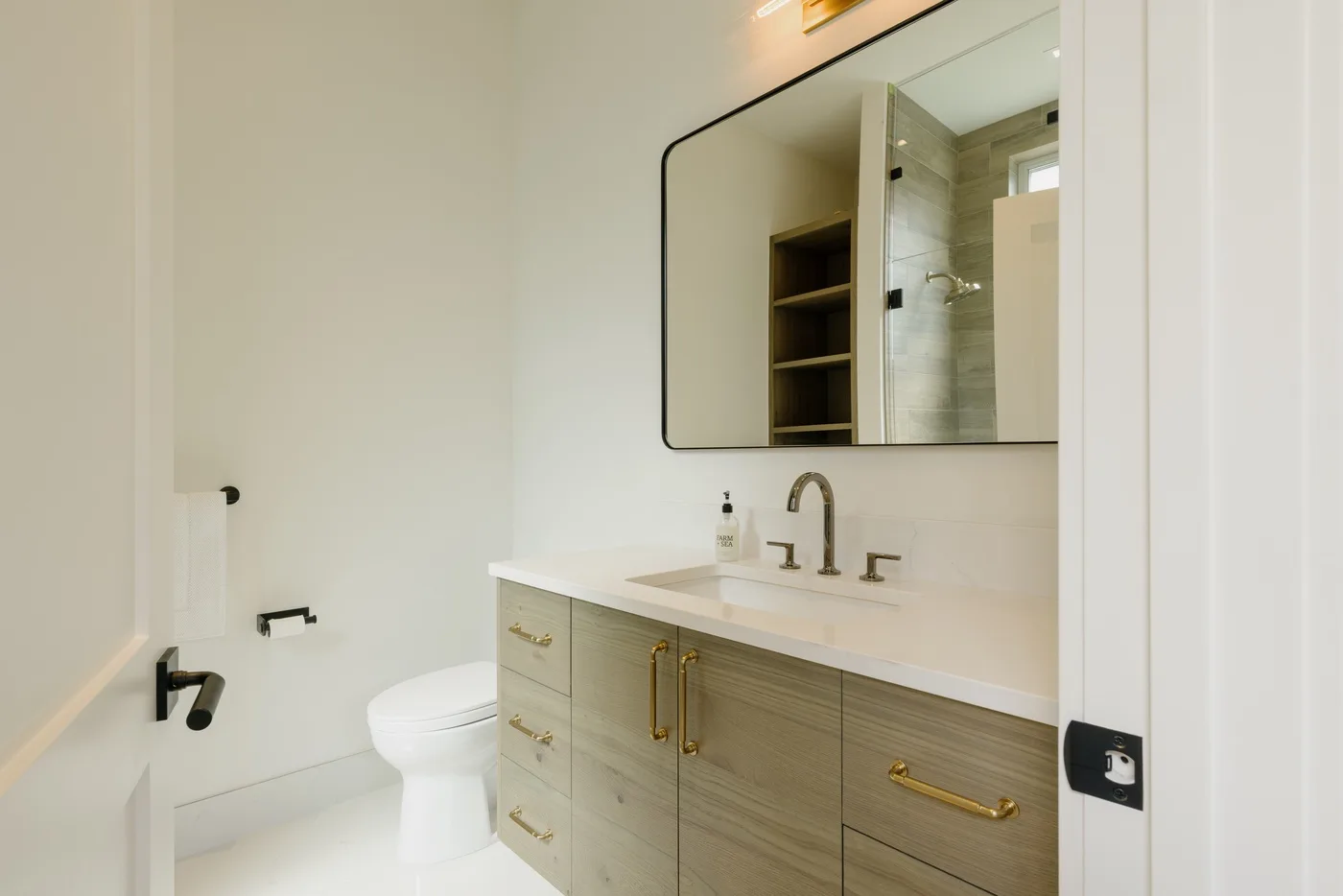 Un baño con mueble de lavabo en tono madera y un gran espejo.