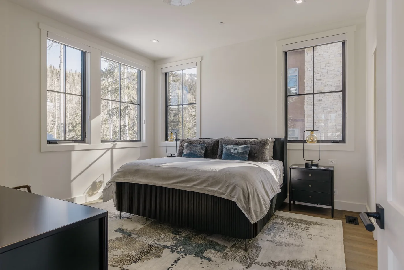 Un dormitorio luminoso con una cama bajo varias ventanas grandes.