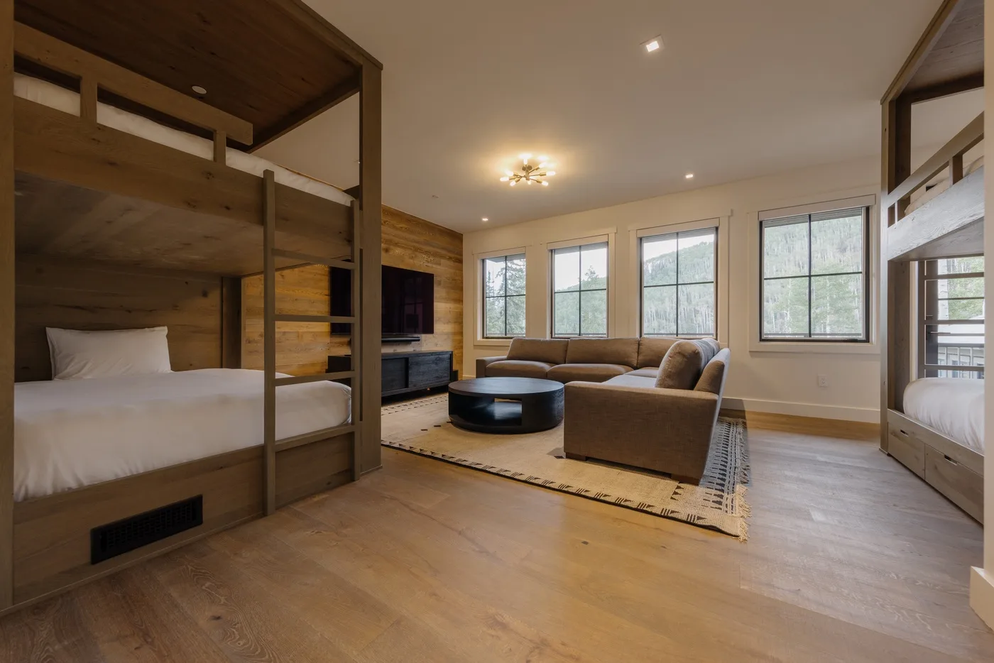 Un dormitorio con zona de estar, literas, asientos y ventanas grandes.