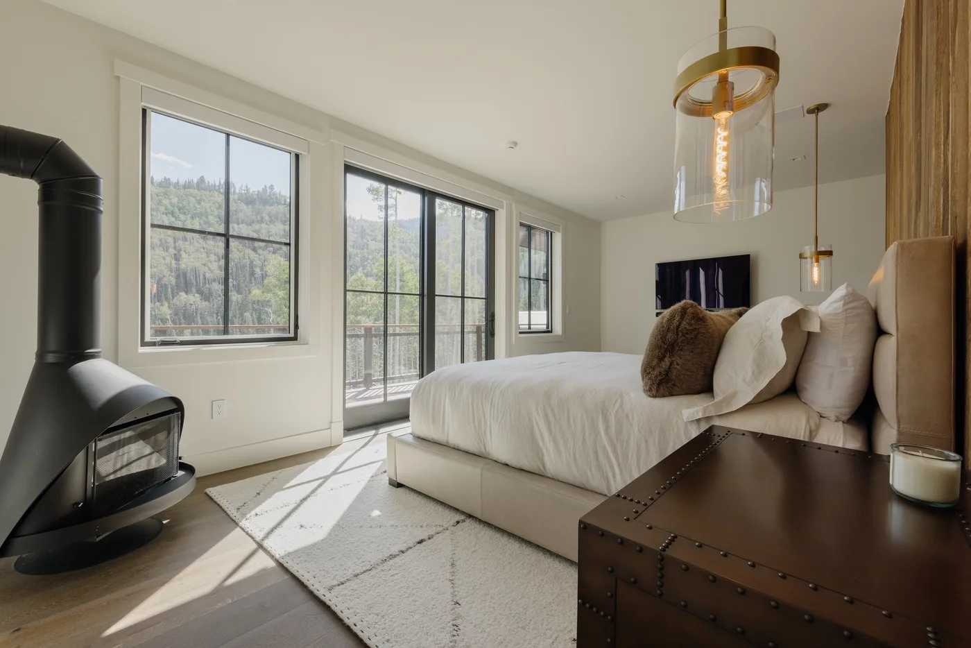 Un dormitorio luminoso con una cama junto a grandes ventanas y una estufa negra.