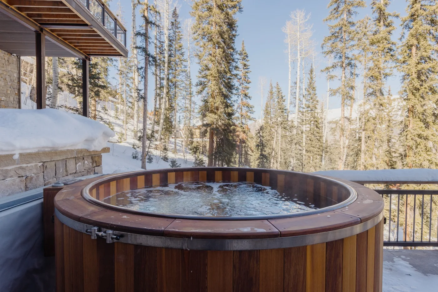 Una bañera de hidromasaje redonda está en una terraza nevada rodeada de árboles.