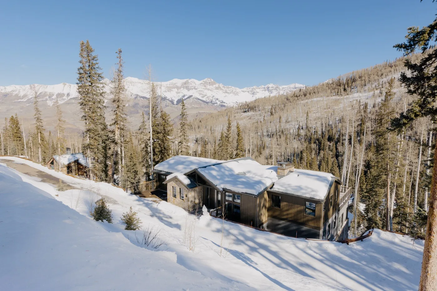 Una cabaña cubierta de nieve está entre árboles, con una cordillera al fondo.