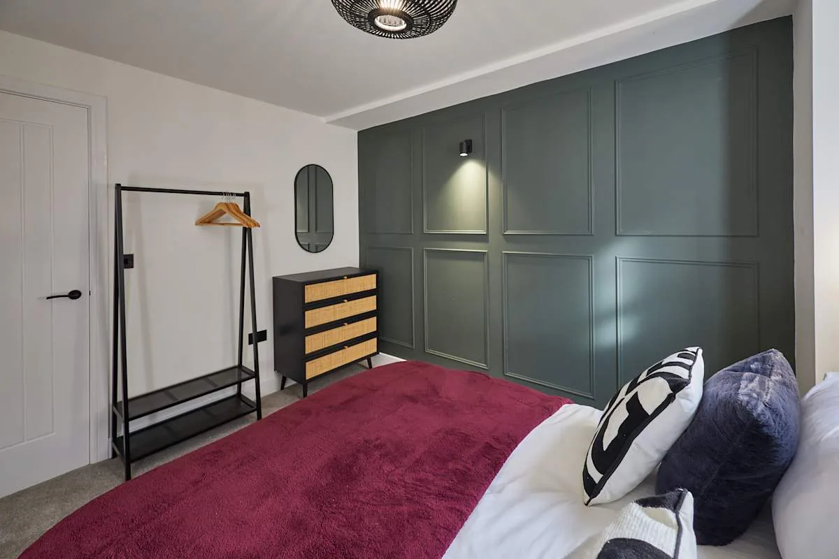 Dormitorio con una alfombra magenta y una pared oscura con paneles.