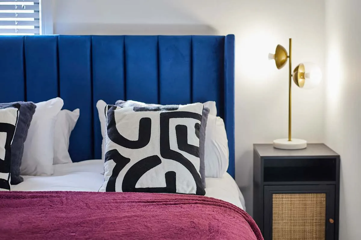 Dormitorio con cabecero azul tapizado y cojines estampados.