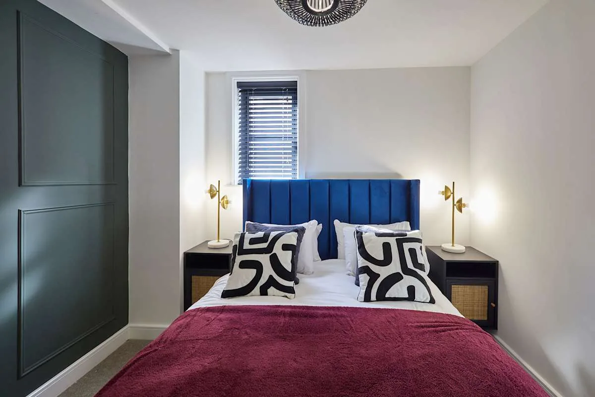 Dormitorio con cabecero azul tapizado y cojines estampados.