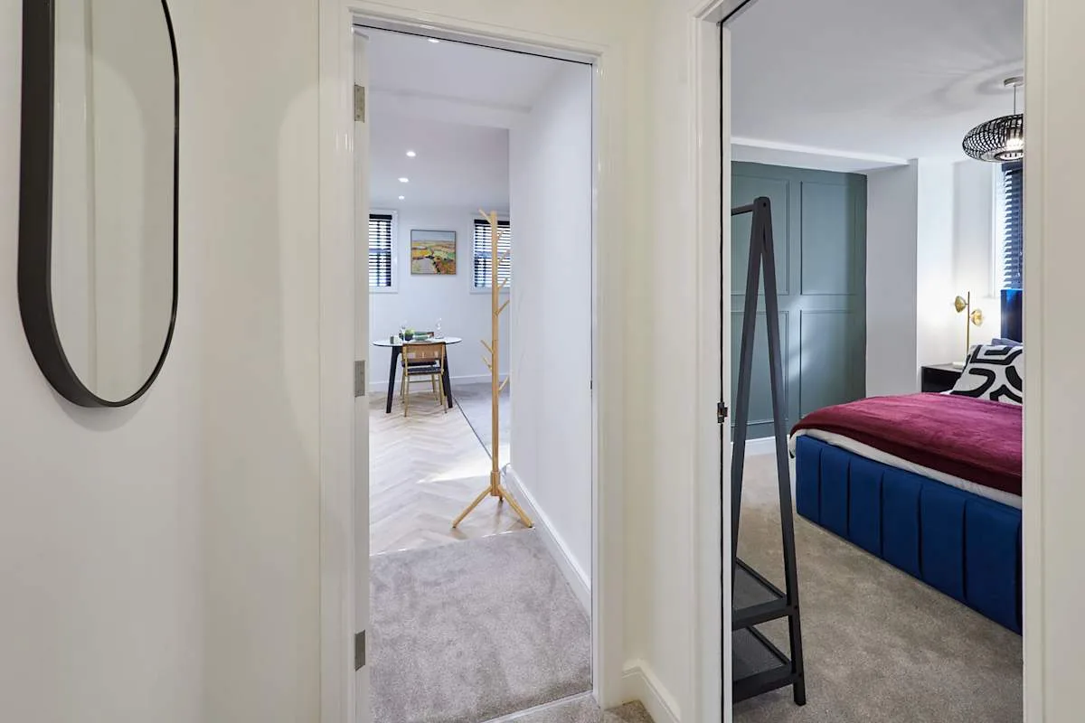 Se ve un dormitorio con una cama azul y ropa de cama magenta a través de la puerta.