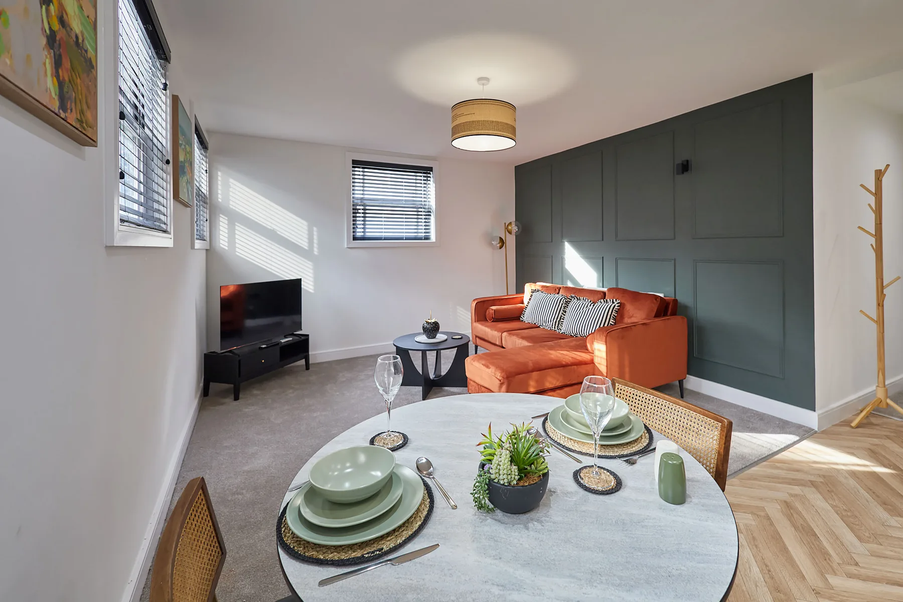 Una sala de estar con un sofá naranja, televisor y una mesa puesta con platos.