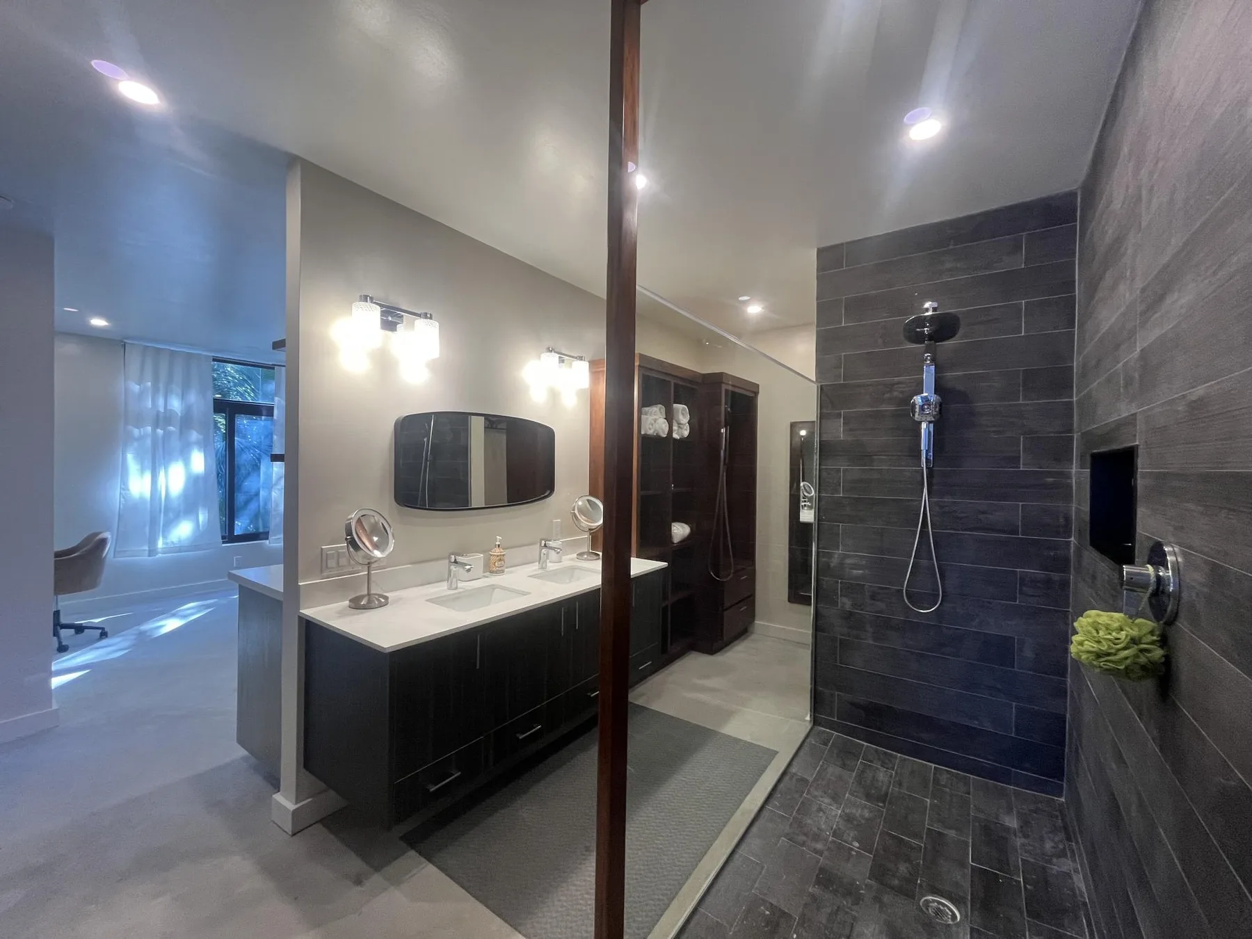 A modern bathroom with a double vanity and a dark-tiled shower area.