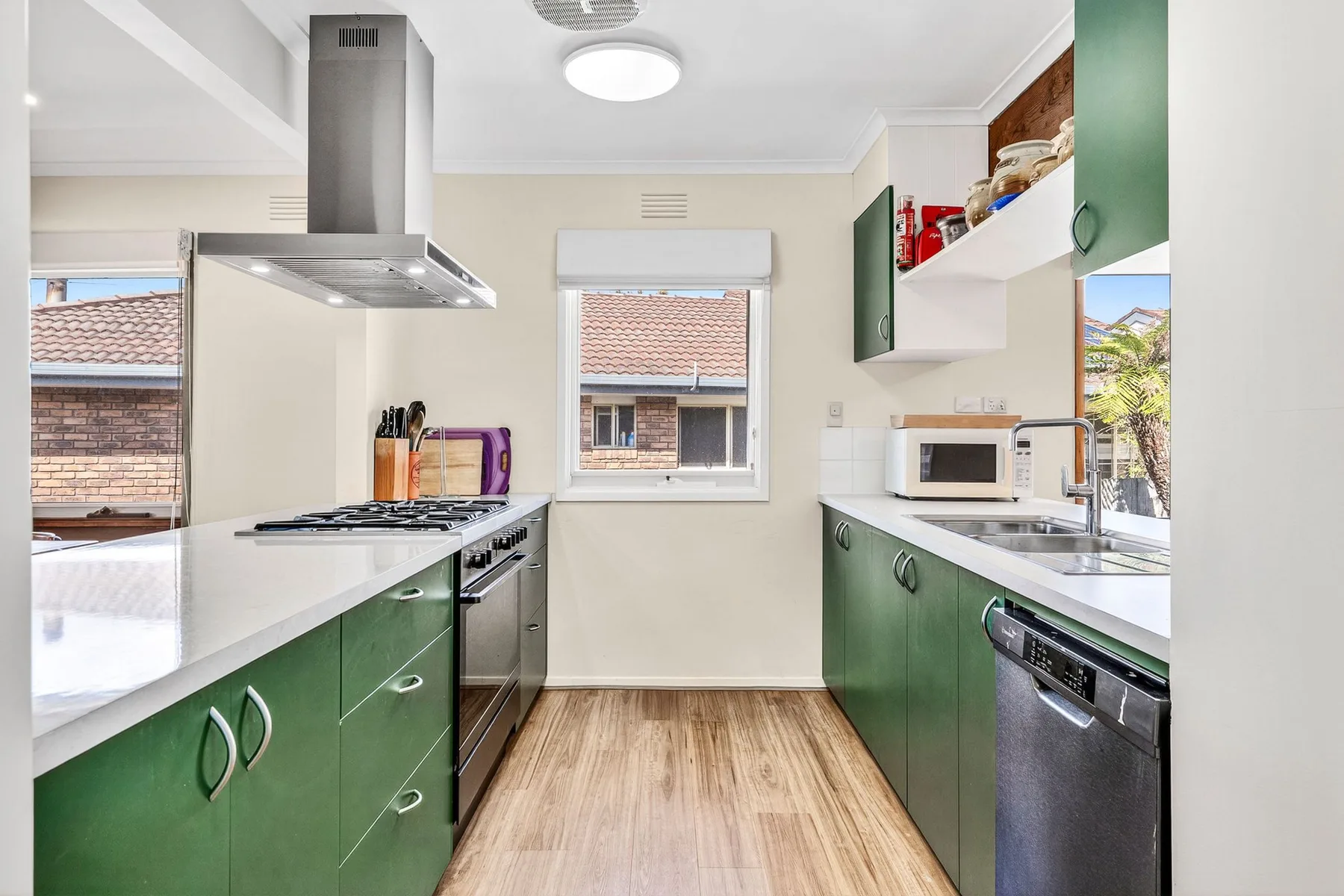 Una cocina luminosa con gabinetes verdes, encimeras blancas y una ventana central.