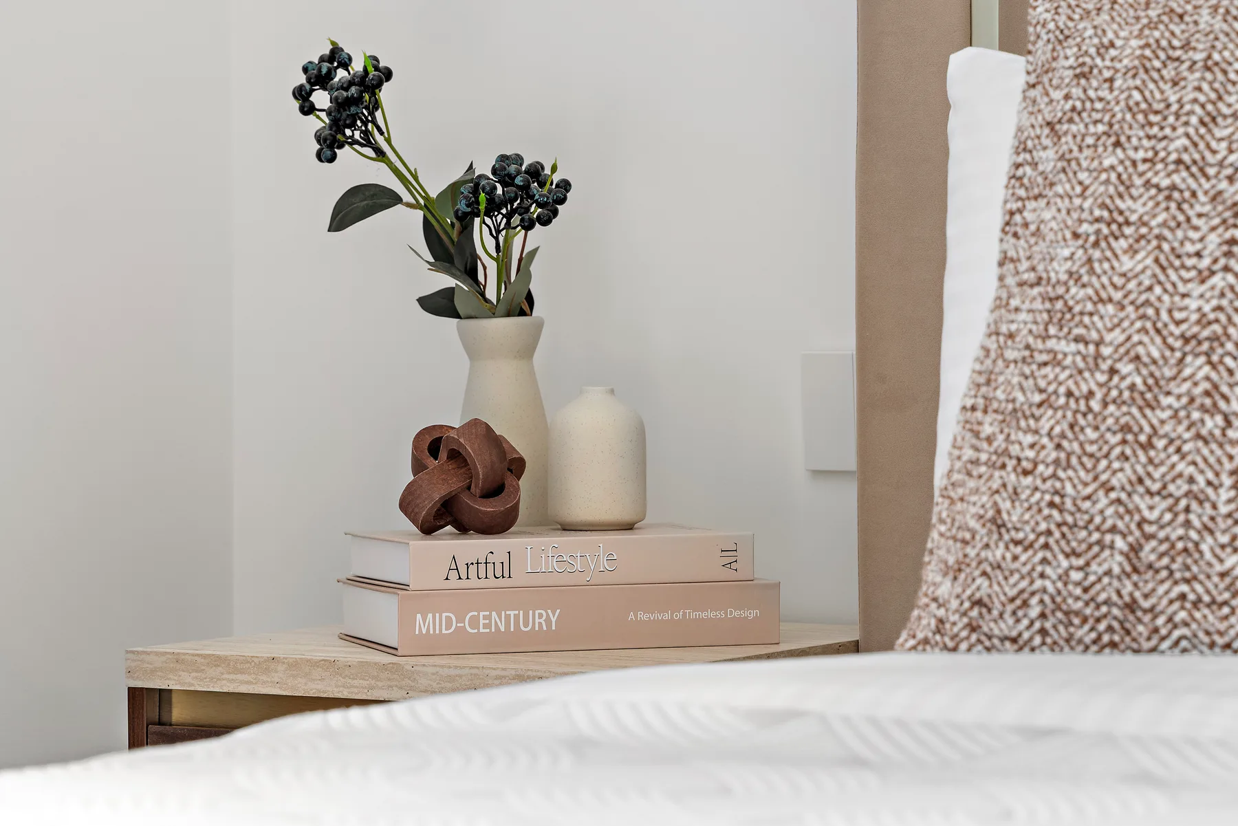 Una mesa junto a la cama muestra un jarrón con flores y objetos decorativos.