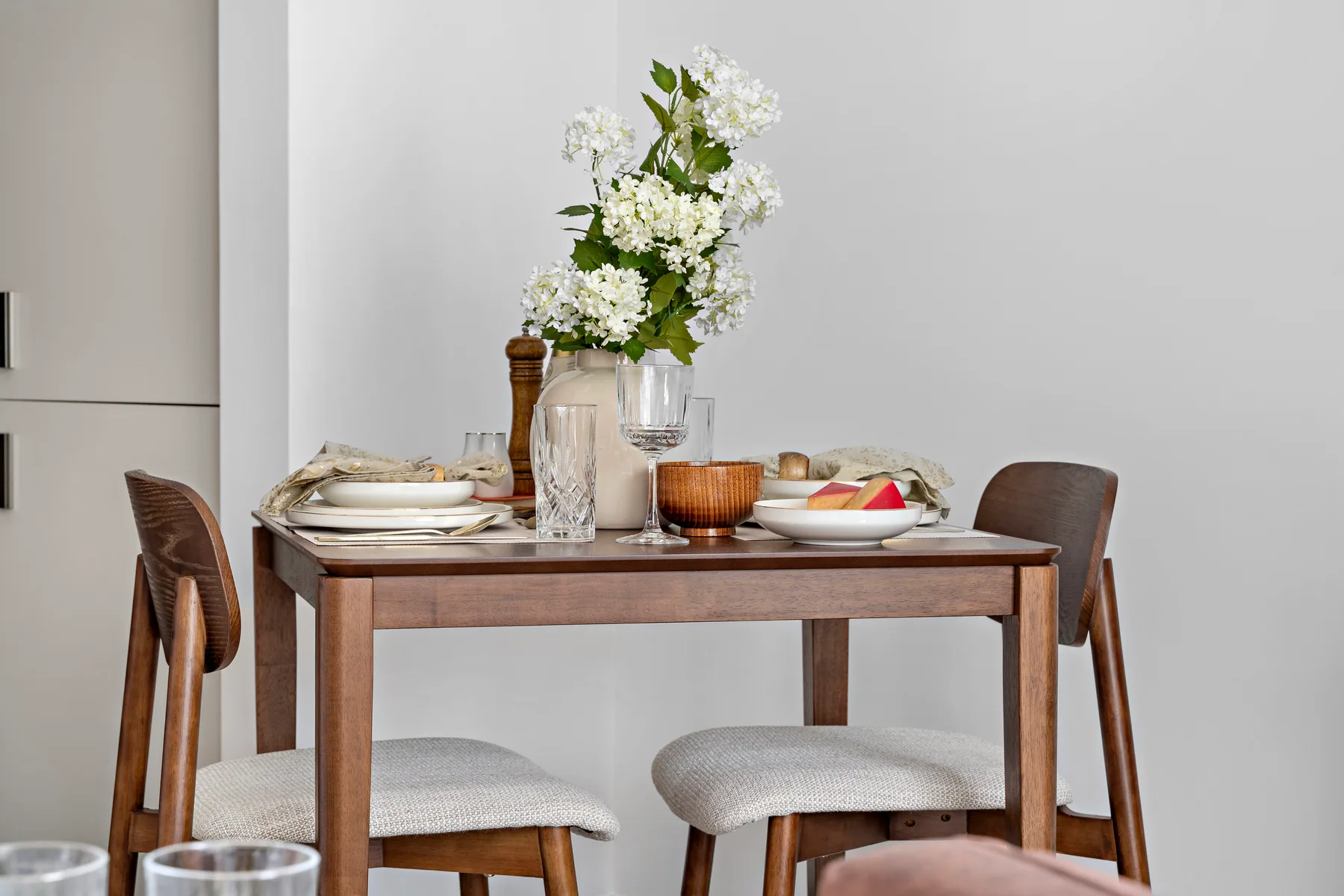 Una mesa de comedor está puesta con platos, vasos y un florero con flores.