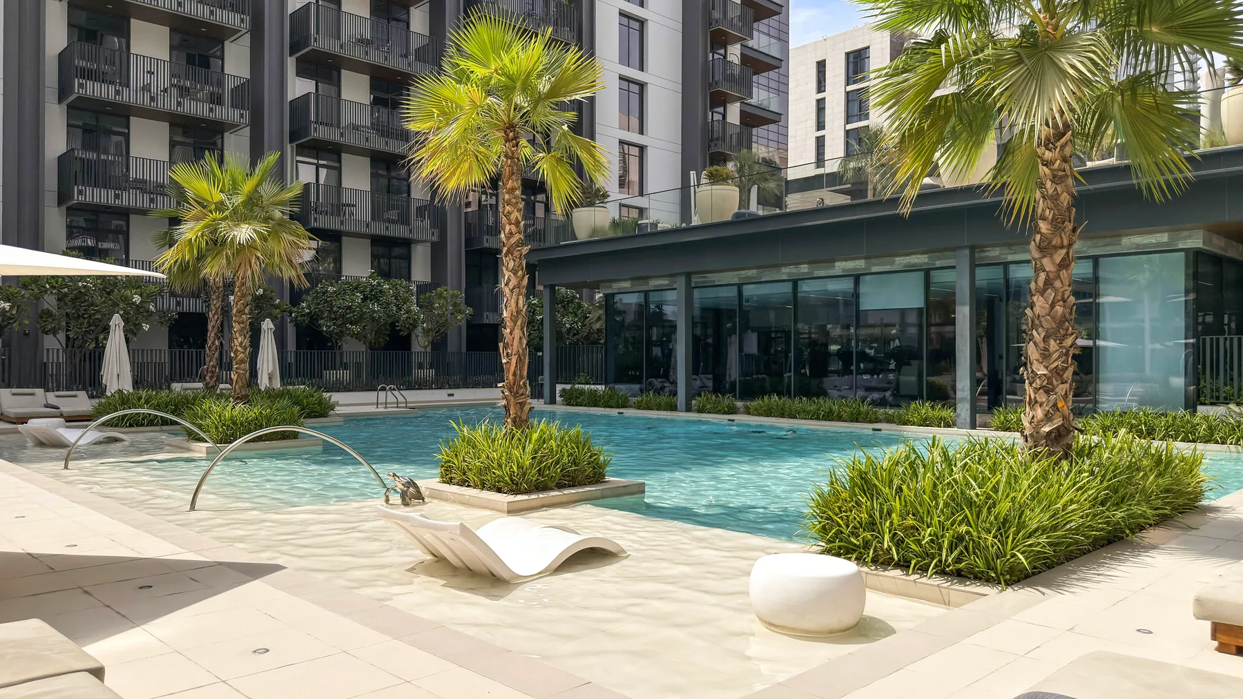 Una piscina al aire libre rodeada de palmeras y un edificio moderno.