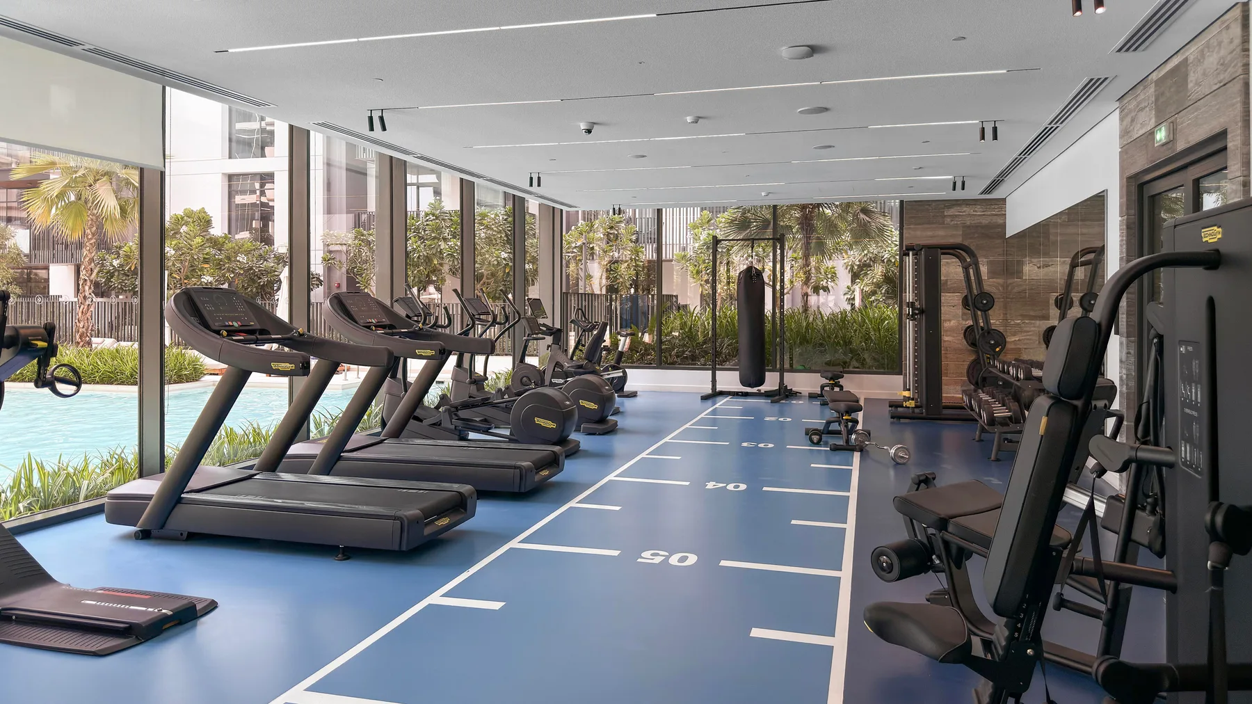 Un gimnasio luminoso con cintas de correr junto a una pista azul.