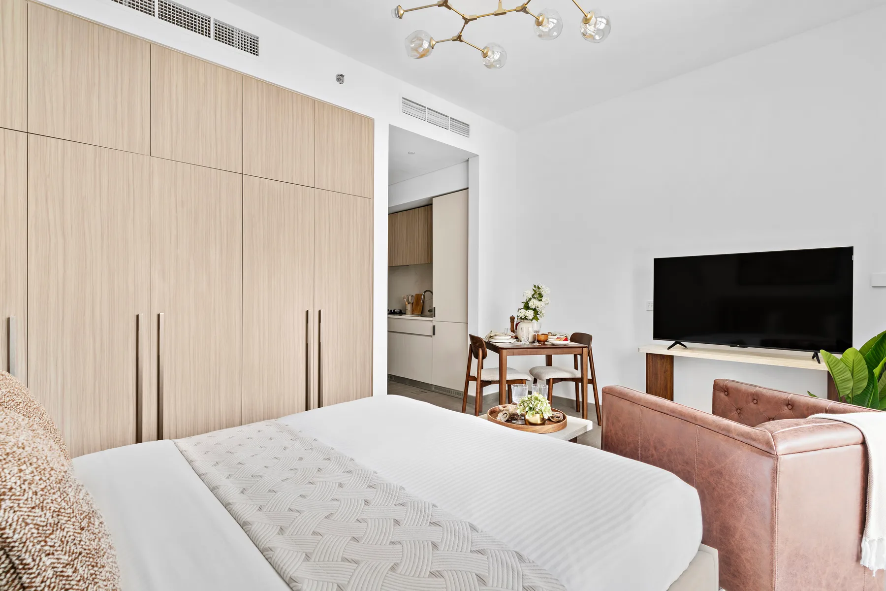 Un dormitorio luminoso con una cama, un televisor y armarios de madera clara.