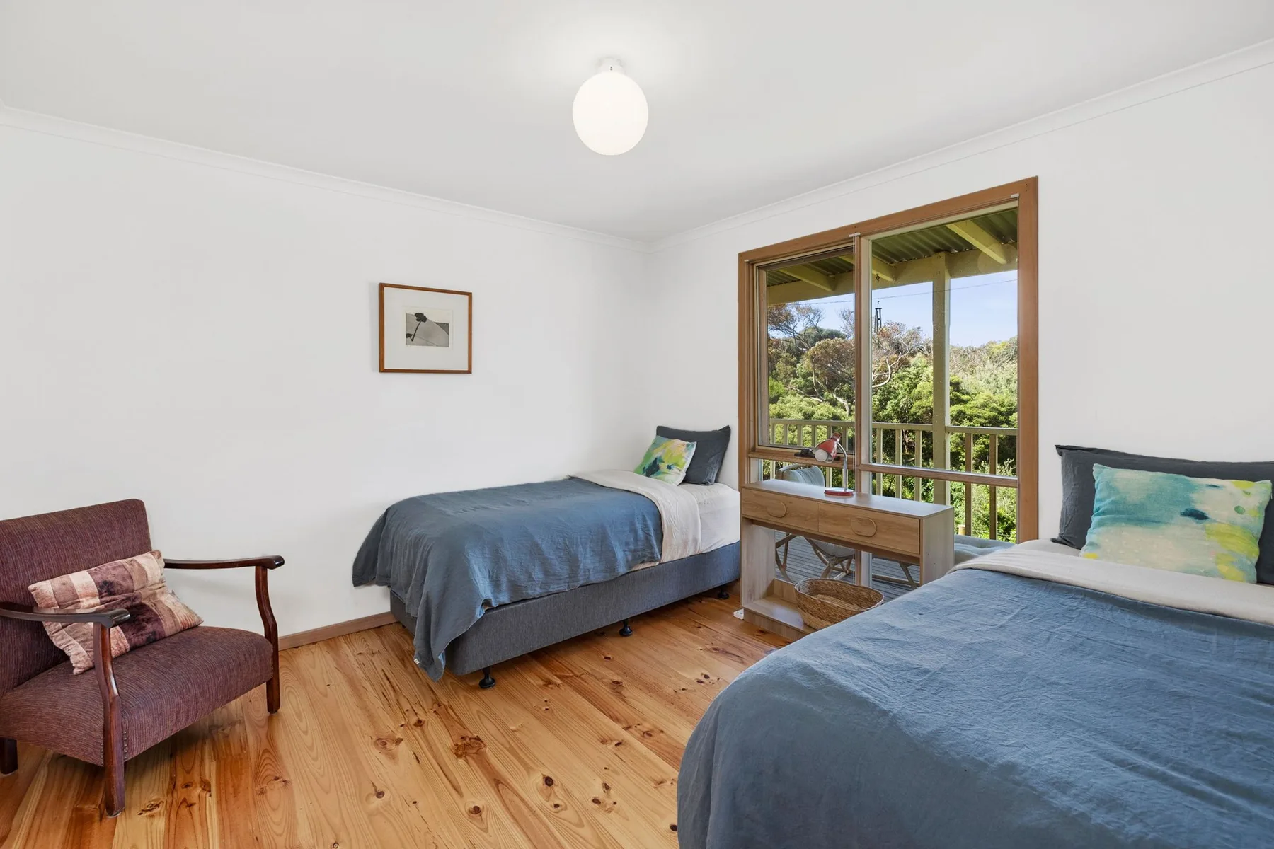 A bedroom with two beds and a window overlooking greenery.