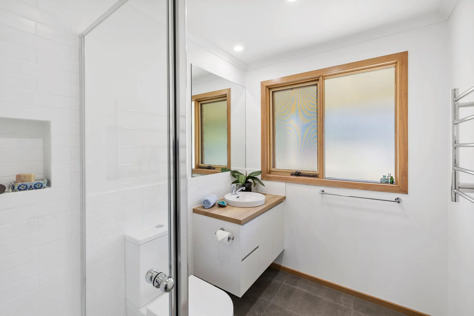A bright bathroom with a glass shower and a vanity beneath a window.