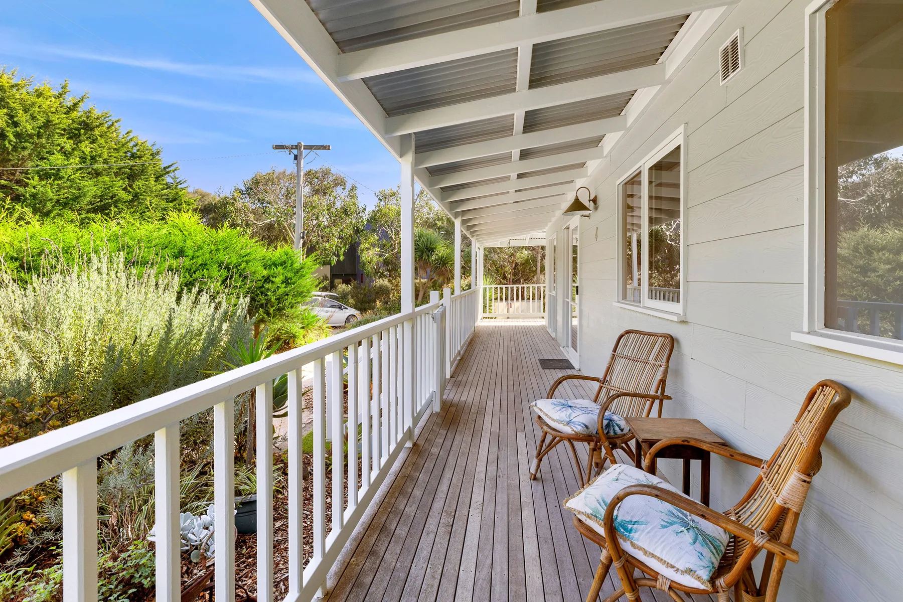 A covered porch with outdoor seating overlooks leafy greenery.