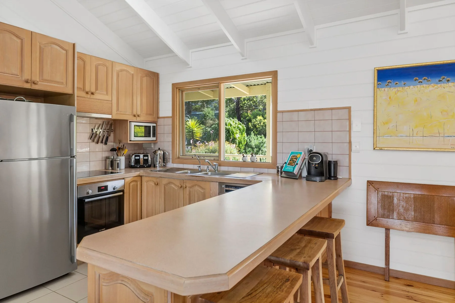 A bright kitchen with a long island and a window overlooking greenery.