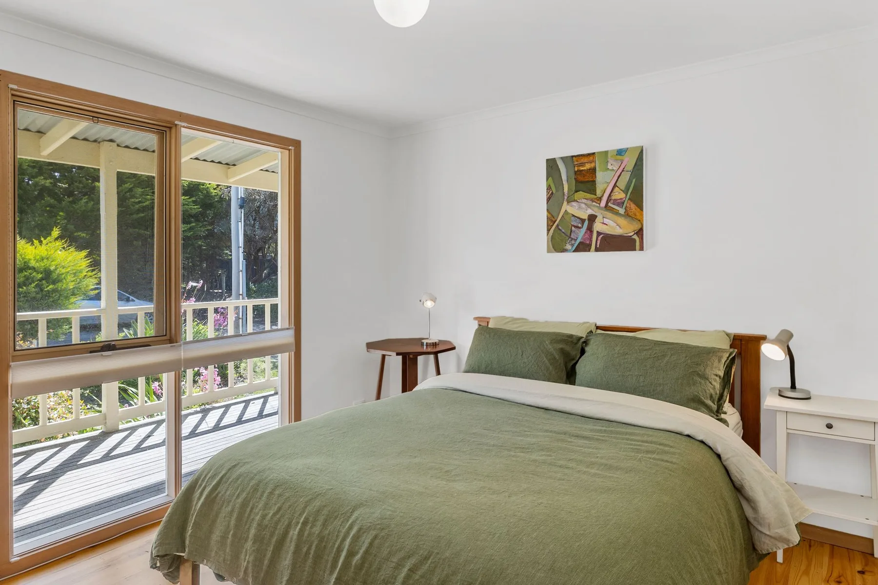 A bedroom with a green bedspread, bedside tables, and a large window.