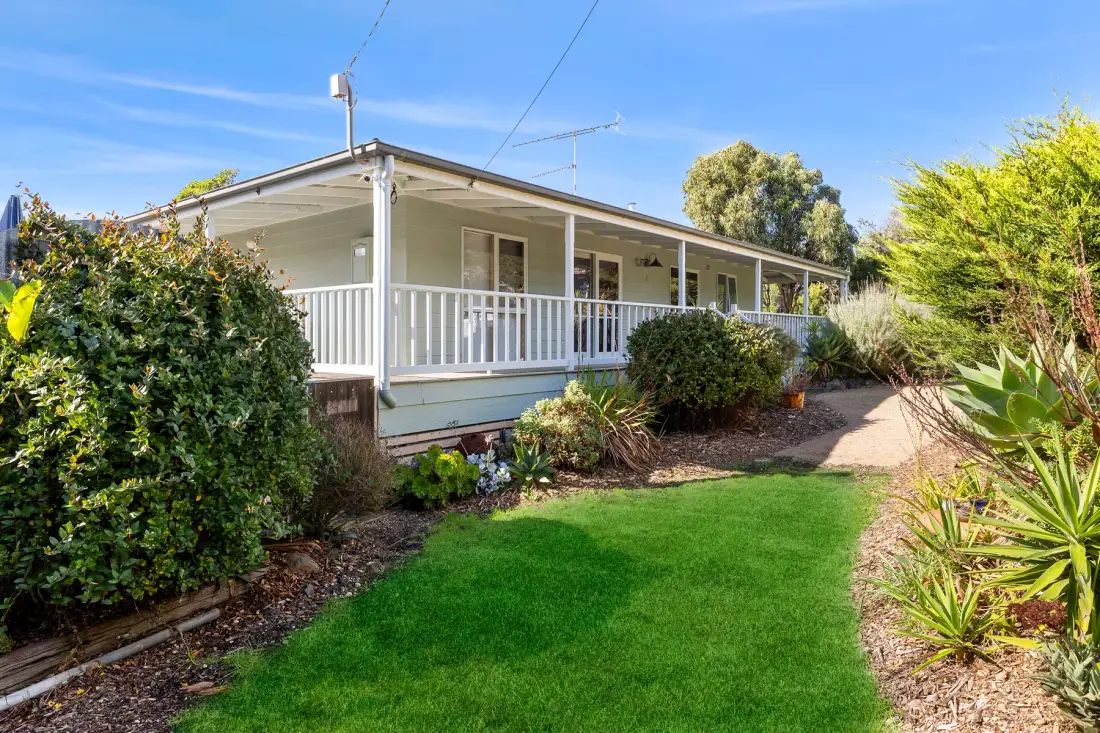A single-story house with a white-railed porch faces a green lawn.